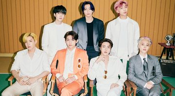 Quatro integrantes do BTS sentados em cadeiras perto um do outro; o resto do grupo posa em pé atrás dos colegas  (Foto: Divulgação / Instagram oficial)